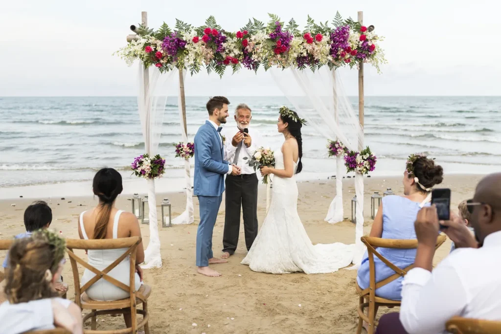 A picture of a couple getting married in front of the ocean, with an alter covered in flower garlands.