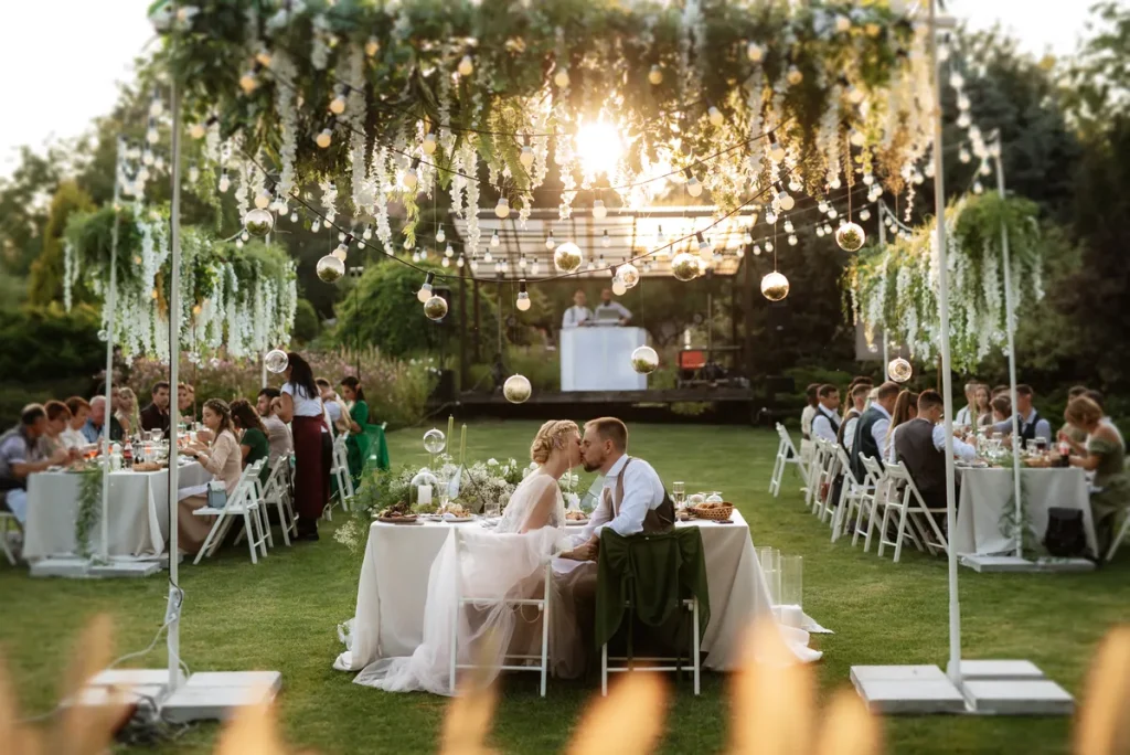 A picture of a small, backyard wedding with the couple kissing, flowers and fairy lights everywhere.