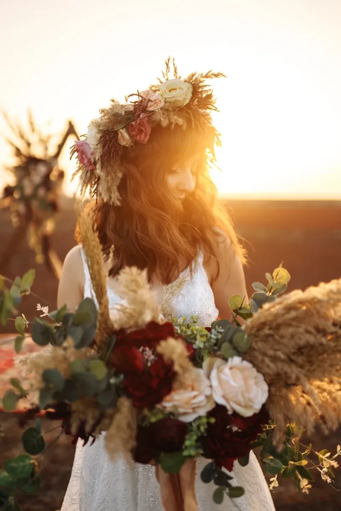 A lovely picture of a bride in front of a sunset, dressed in a flower crown and a very boho wedding dress.