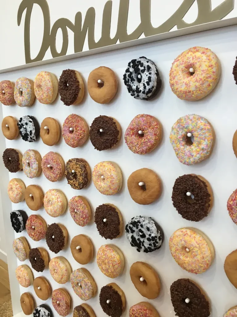A donut wall with all different kinds of donuts on display for wedding guests to grab as they want one.