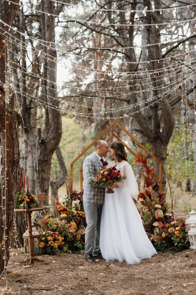 A picture of a rustic wedding in the woods, with fall colored flowers and candles around.
