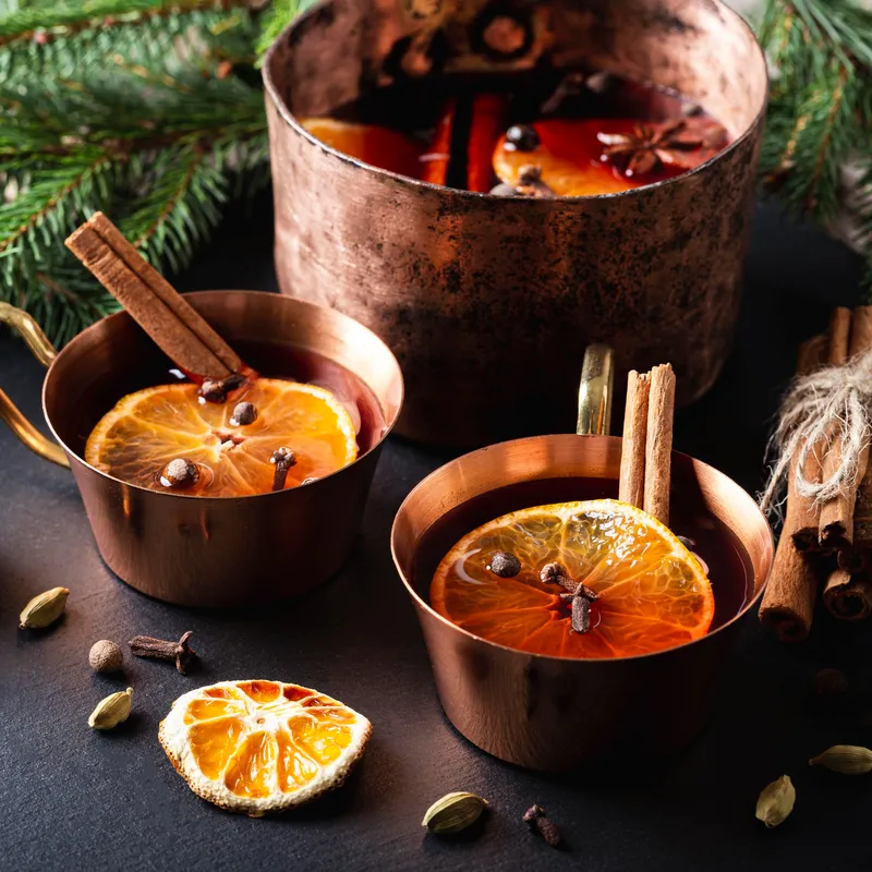 A picture of a large pot of mulled wine and two cups full with some lovely garnishes.