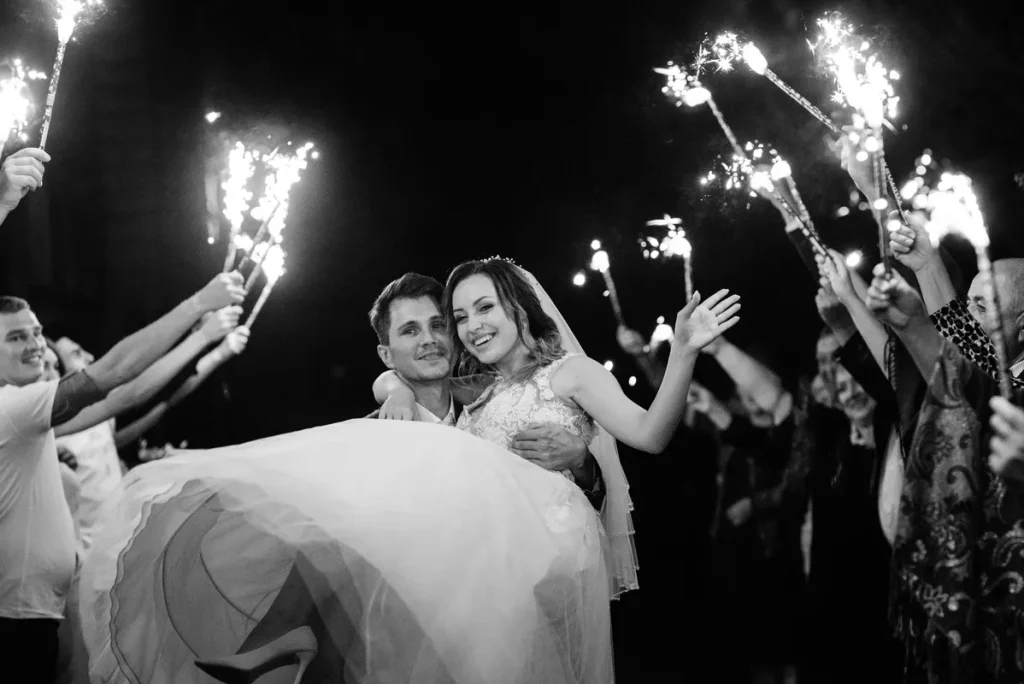 A couple who just got married, the groom carrying the bride down the isle at 12 on new years with the guests waving sparklers around them.