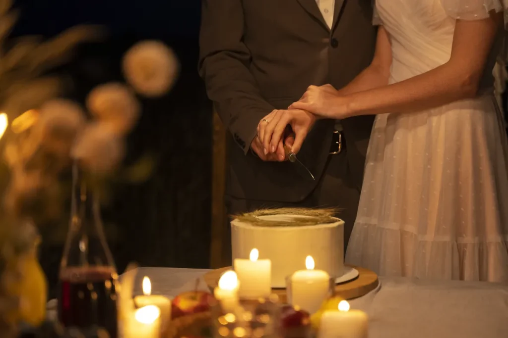 A picture of a couple cutting their wedding cake in front of some candlelight.