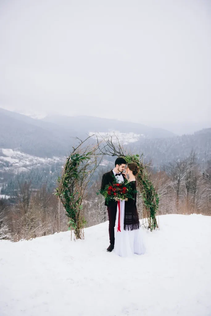 A picture of a beautiful outdoor ceremony with an evergreen arch and a happy couple in front of it.