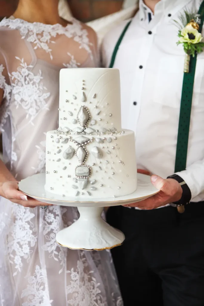 A white wedding cake with silver fondant details.