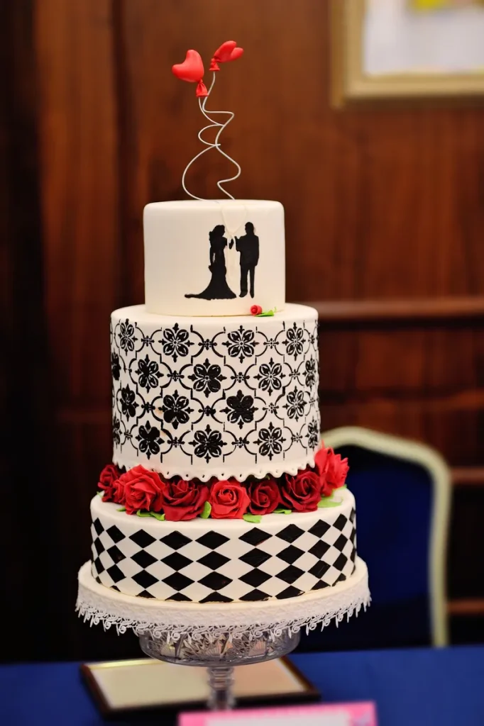A black and white cake with some red rose detailing.
