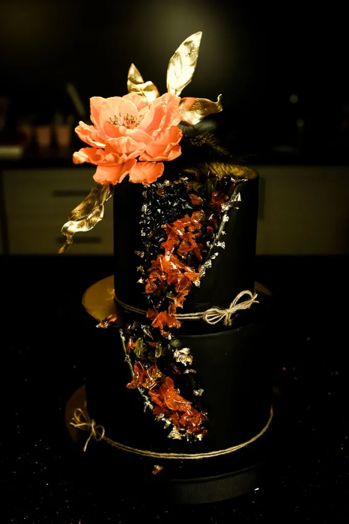 A black geode cake with reddish pink details and a flower.
