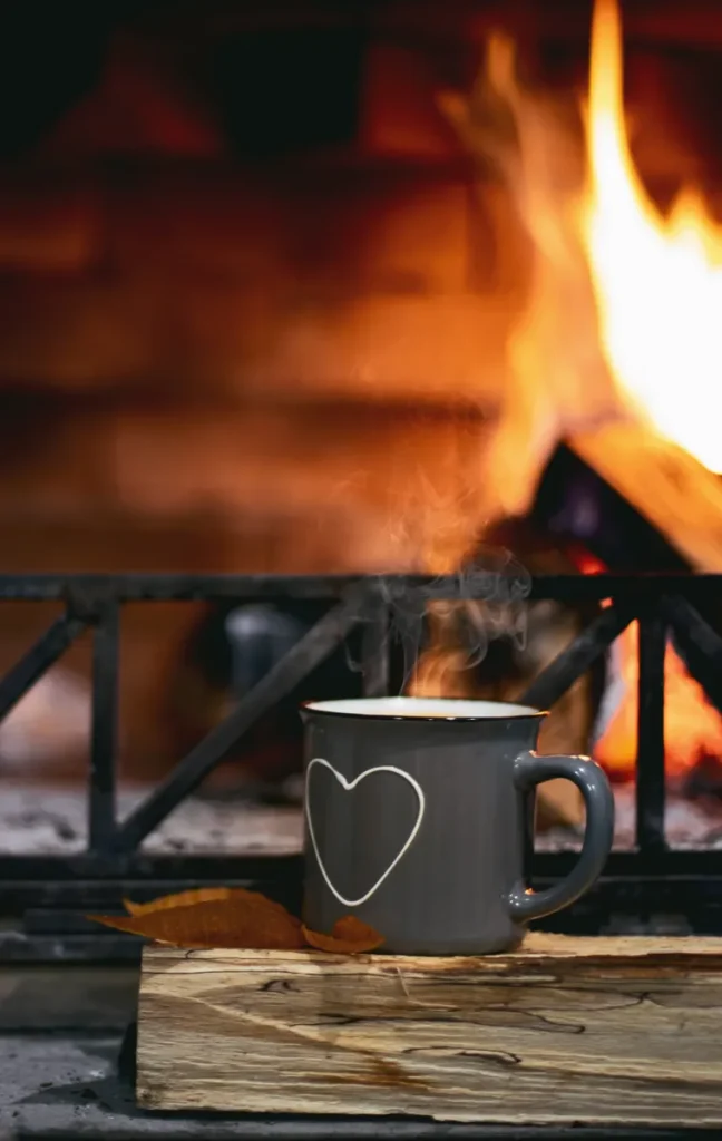 A roaring fireplace with a mug in front that has a heart on it.