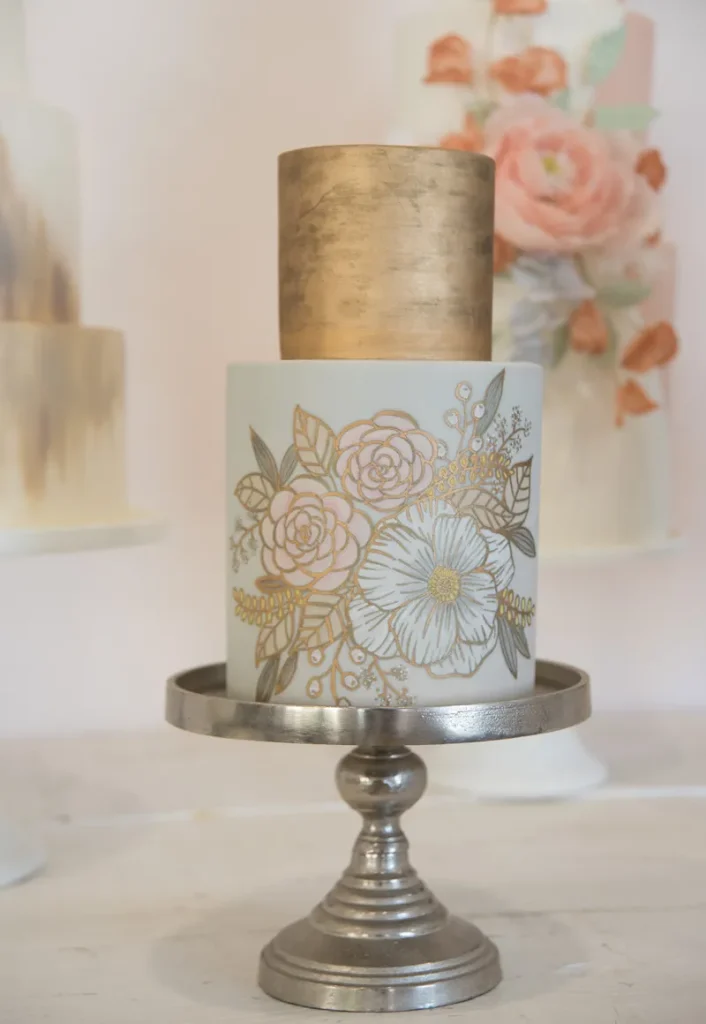 A two tier cake with gold leaf and flowers stenciled on.